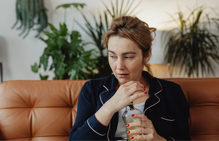 Worried woman holding a drink on the couch, contemplating whether to quit or cut back on alcohol.