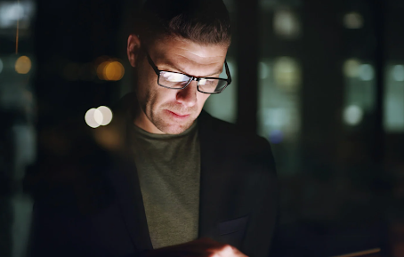 Man in business attire looking down at a screen at night, symbolising the hidden nature of high functioning drug users who appear professional and composed.