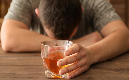Man showing the long term impacts of alcohol with head down holding glass of alcohol
