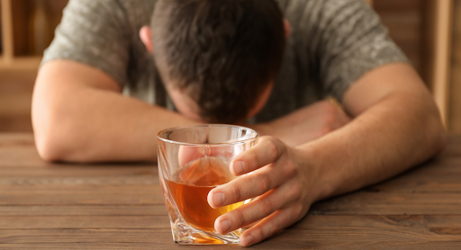 Man showing the long term impacts of alcohol with head down holding glass of alcohol