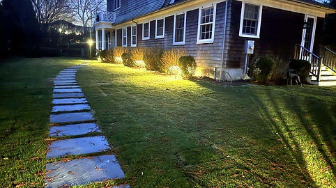 Shingled house at dusk with security cameras and landscape lighting in the Hamptons