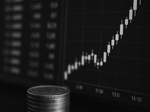 Stacked coins in front of a rising line graph on a dark screen, suggesting financial growth. The background is blurred.