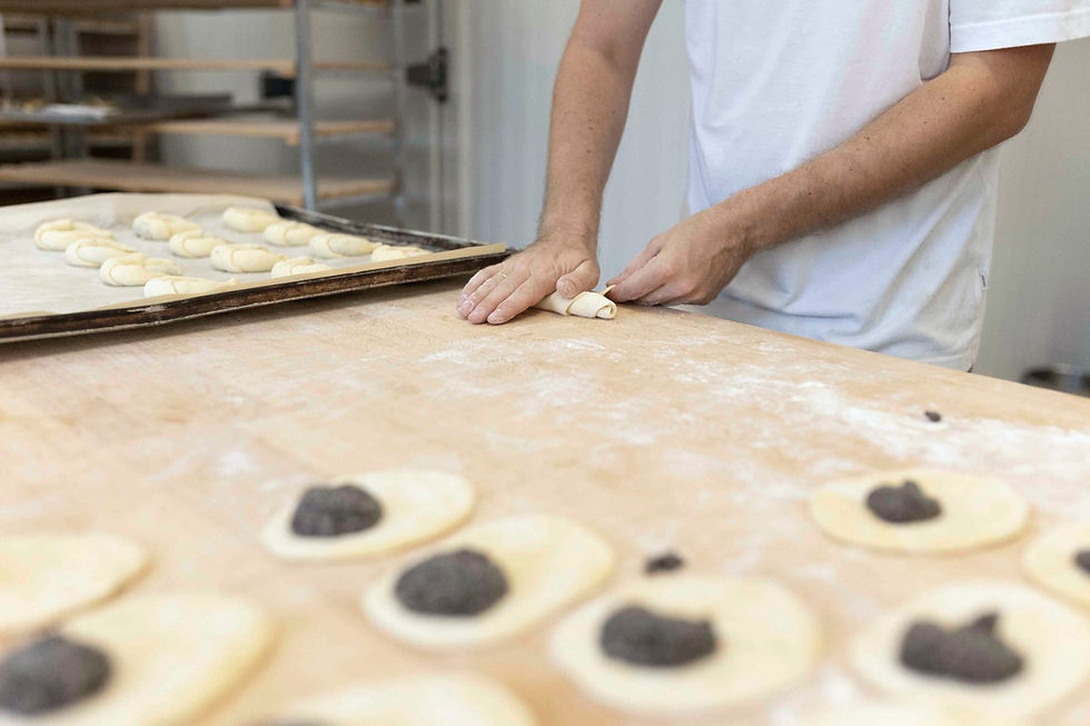 In der Backstube auf einer Holzarbeitstafel rollen Hände ein Kipferl. Jeder Schritt ist Handarbeit.
