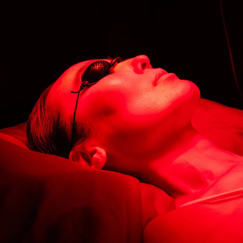 Person lying back under red light wearing dark goggles, face up on a table against a black background.