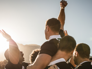 A group of teammates cheering and lifting a leader in celebration under a bright sun to represent peak professional achievement