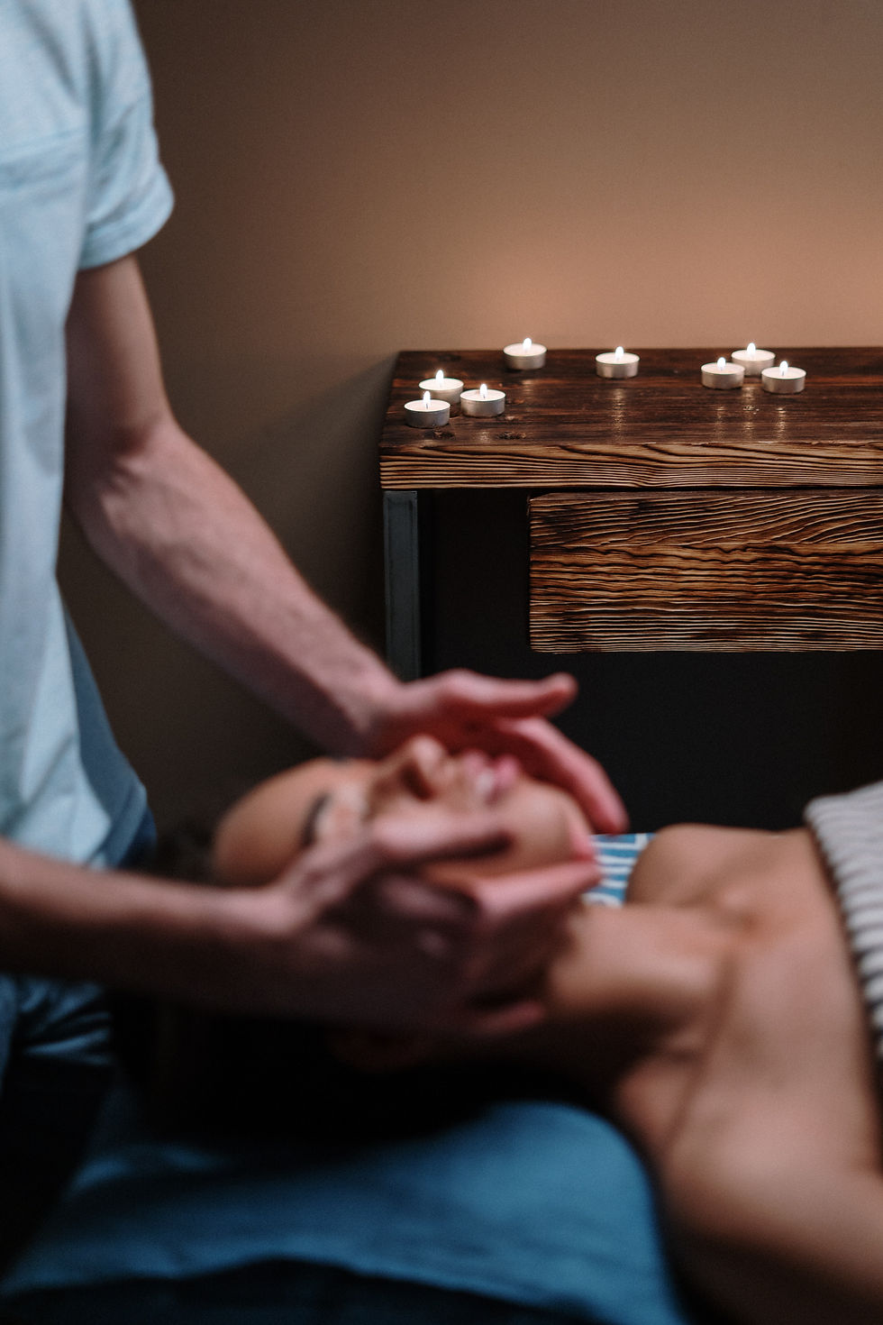 une personne masse le visage d'une femme dans une ambiance chaleureuse avec des bougies et une détente absolue