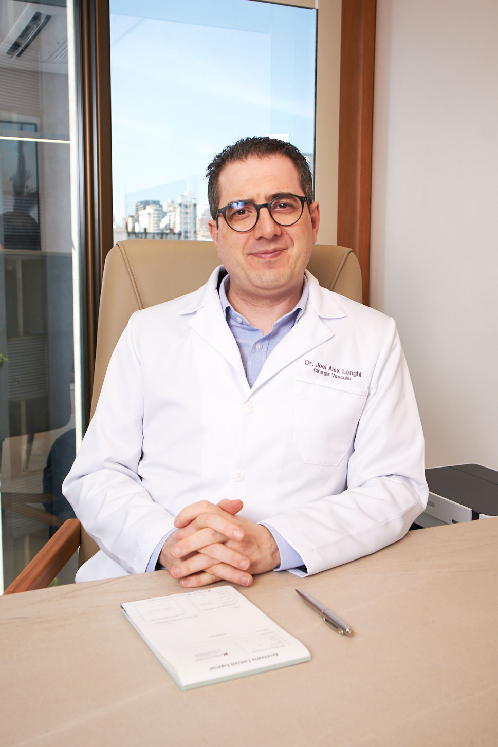 Retrato em consultório, médico de jaleco branco sentado à mesa, tons neutros, portrait