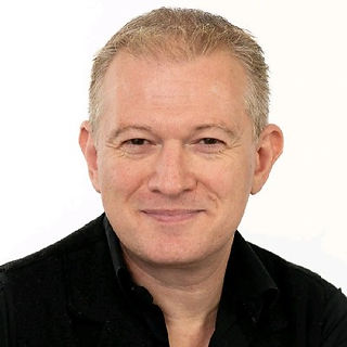 A smiling man with a white/beige background.