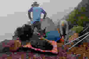 German shepherd dog lies on travel dog bed while man and woman set up text on mountainside.