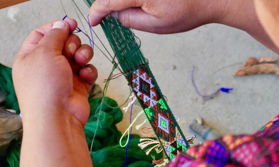 Indigenous Guatemalan artisan woman weaves típico ribbon on back strap loom