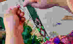 Indigenous Guatemalan artisan woman weaves típico ribbon on back strap loom
