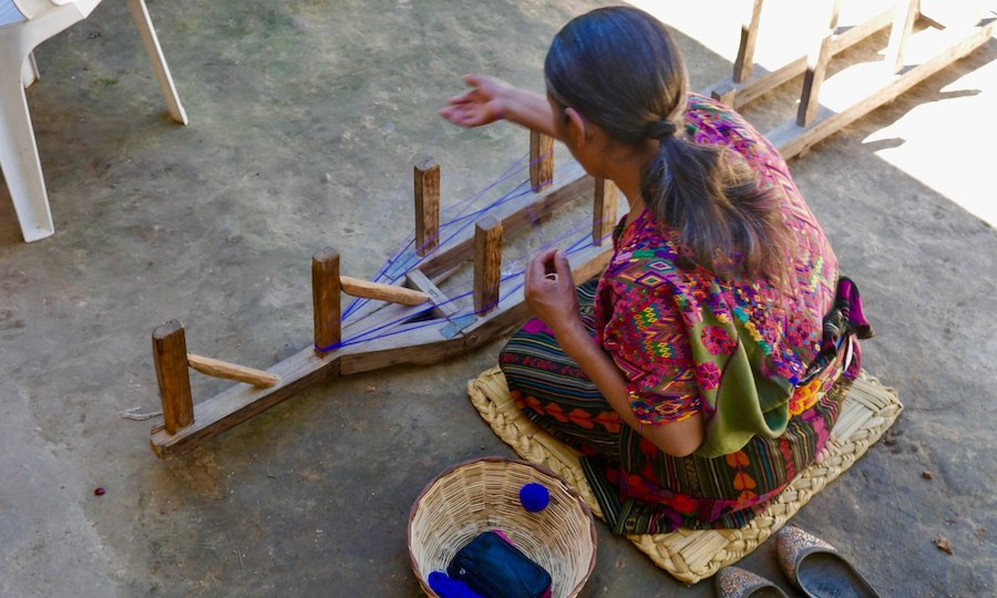indigenous Guatemalan artisan sits on ground to weave