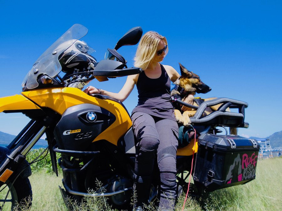 Woman leans against motorcycle with dog in carrier