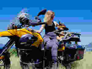 Woman leans against motorcycle with dog in carrier