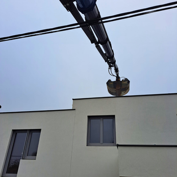Kran Arm beim aufheben von Schotter auf ein Flachdach eines Neubaus über eine Stromleitung.