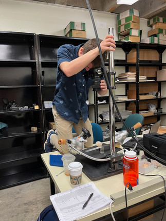 Chandler Olson photographing shells in the UF collection. The shell is large so he stands on the table to get it all in frame.