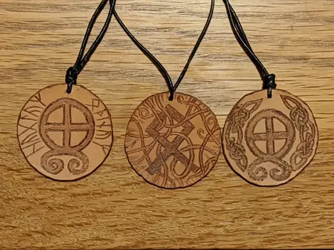 three round leather pendants on leather cords on an oak table featuring runes and symbols 