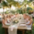 Outdoor event photography of a long, elegantly set banquet table with guests seated under palm trees. The scene suggests a warm, celebratory evening gathering.