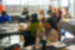 People are seated at tables in the space, taking in a presentation.