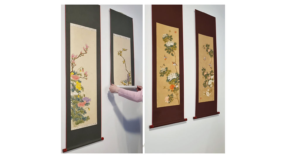 Two sets of painted scrolls are shown side-by-side. The set on the left, with green fabric, has paintings in soft, pastel colors. The set on the right, with brown fabric, features a painting with rich greens and red birds.