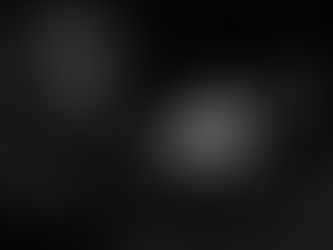 Schwarz-weiß Fotografie eines Schützen beim Training in einer Indoor-Schießanlage. Der Mann trägt Gehörschutz und Schutzbrille, hält eine Pistole im Anschlag und konzentriert sich auf eine Zielscheibe im Hintergrund.