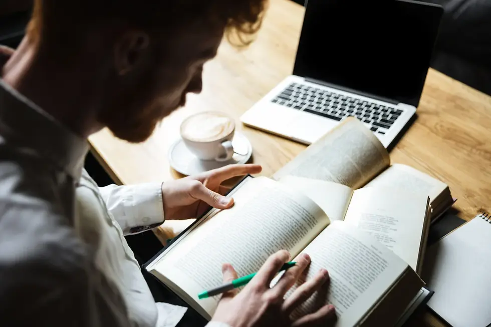 Homem lendo a bíblia, com um café e um notebook sobre a mesa, simbolizando como conciliar estudos e trabalho.