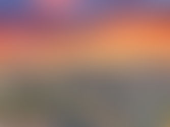 Aerial view of a city skyline at sunset with vibrant orange and pink clouds. Buildings and streets are visible, with mountains in the distance.