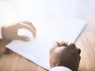 Hands write on blank paper at a sunlit wooden desk, with soft bright light and a calm workspace.