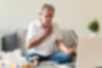 Elderly an holding chest in discomfort, seated on couch with laptop