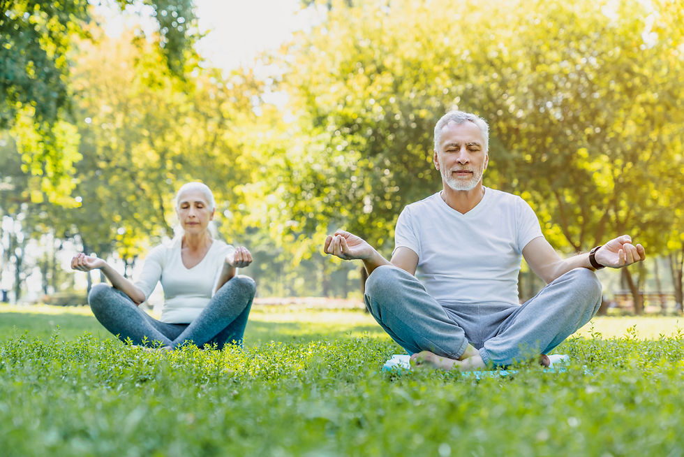 A man and a woman meditating while sitting on the grass in a park