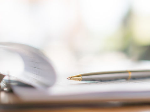 Close-up of a silver pen resting on a notebook, with a blurred page turning in the background.