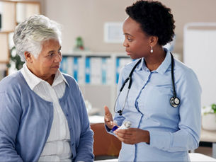 Doctor with stethoscope consults elderly woman in a bright office. They are talking seriously, creating a professional and caring atmosphere.