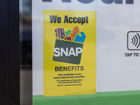 Yellow sign on a glass door reads "We Accept SNAP Benefits" with grocery icons. A contactless pay symbol and "Tap to Pay" are to the right.