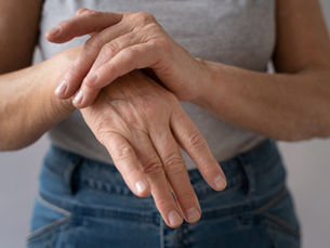 Person pressing their left hand with their other hand, wearing a grey shirt and blue jeans. The scene conveys the person is checking on their hands for pain