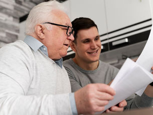 Smiling older man and young man review papers together in a modern kitchen, sharing a warm, focused moment.