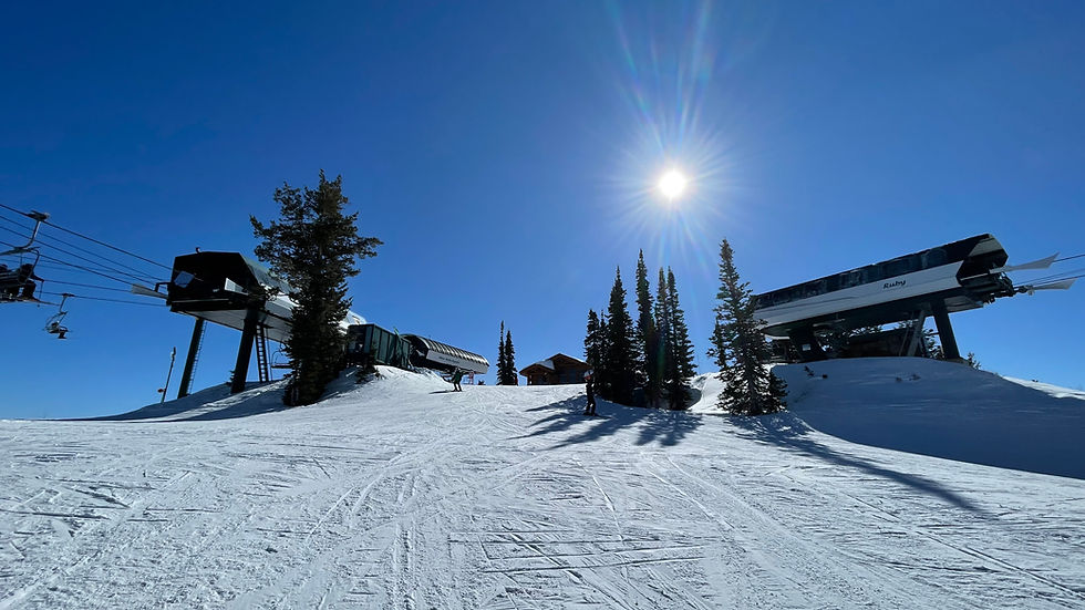Ski lift and trees on a snowy slope under a bright sun and clear blue sky. Sunlight casts shadows on the snow.
