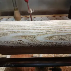 a piece of ash between centres on a woodturning lathe with a worm hole