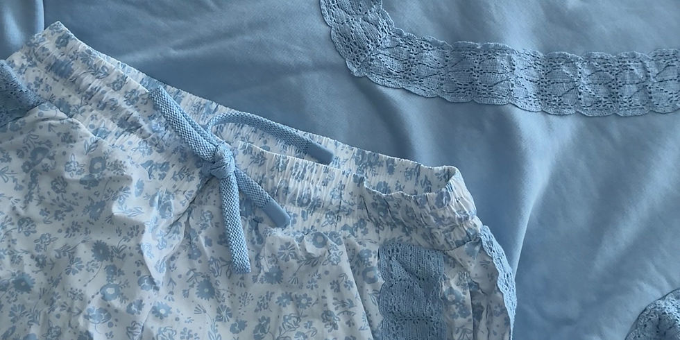 Blue pajama set with lace details on a floral bedsheet. The shorts have a blue floral pattern and a drawstring. Cozy and serene mood.