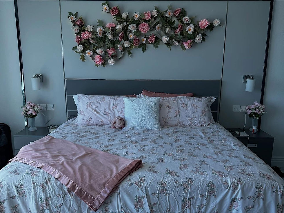 Elegant bed with floral bedding and a pink blanket in a cozy room. Pink and white flower arrangement adorns the headboard, emitting a serene vibe.