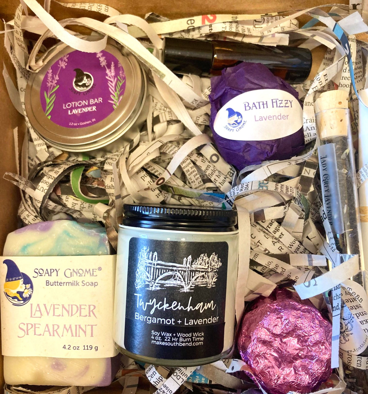 handmade soap, candle in glass jar with metal lid, tin containing lotion bar, tea tube, rollerball, bath bomb, shower steamer