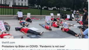 Protesters in red shirts lie on the ground holding signs outside the White House fence. Signs display messages about COVID-19.