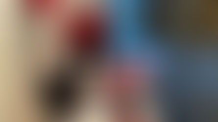 Two people in red shirts stand behind an information table with brochures. The setting is a modern indoor space with white walls.