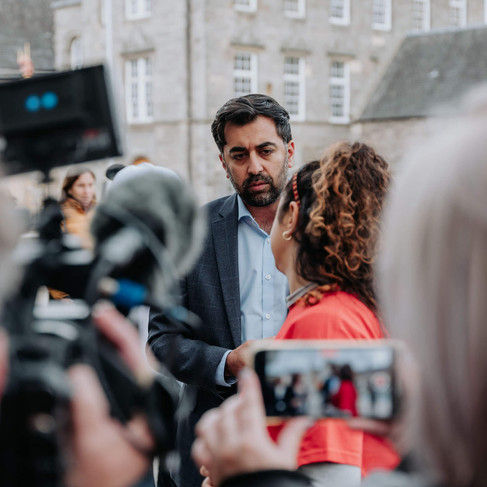 The Scottish Cabinet Secretary for Health, Humza Yousaf, talking to an ME Action Scotland volunteer. In the foreground are press cameras and phones recording them.