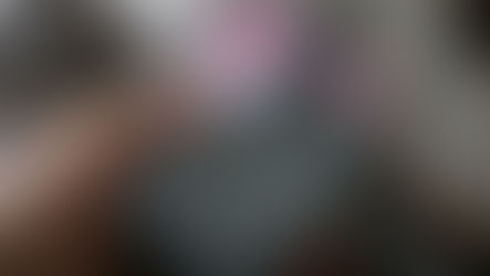 Hand holds a gray remote control pointing at a blurry TV screen. The background is indoors, creating a relaxed, focused mood.