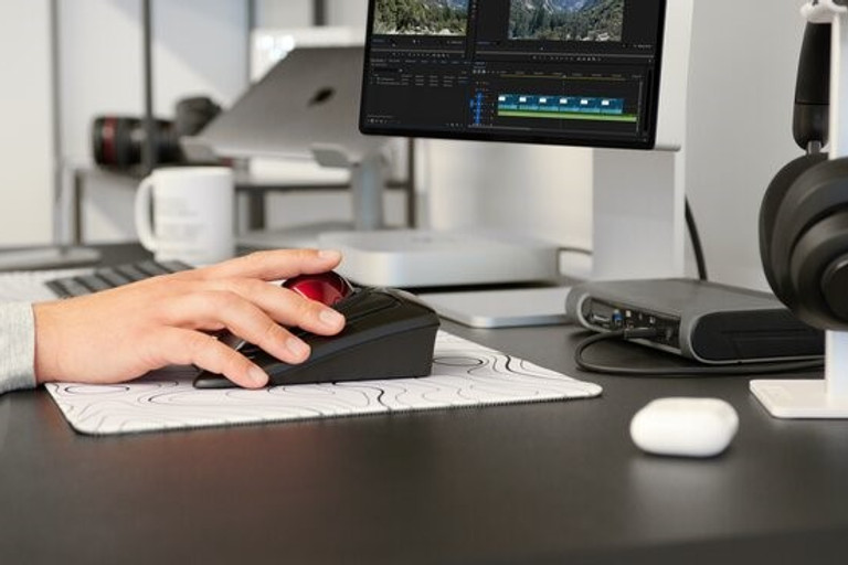 Mano che utilizza un mouse specializzato con pulsante rosso su una scrivania con una timeline di editing video sul monitor