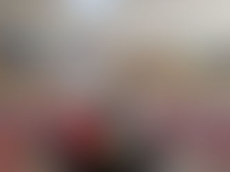 Ein beruhigendes Bild eines Yoga-Raums mit einem Buddha-Statue im Vordergrund, die auf einem farbenfrohen Mandala-Teppich sitzt. Vor der Statue befinden sich eine rote Kerze, ein blauer Stein und ein kleiner Gong auf einem Tablett. Im Hintergrund sind Yogamatten mit Kissen für eine entspannte Praxis sichtbar, während natürliches Licht durch ein Fenster hereinstrahlt