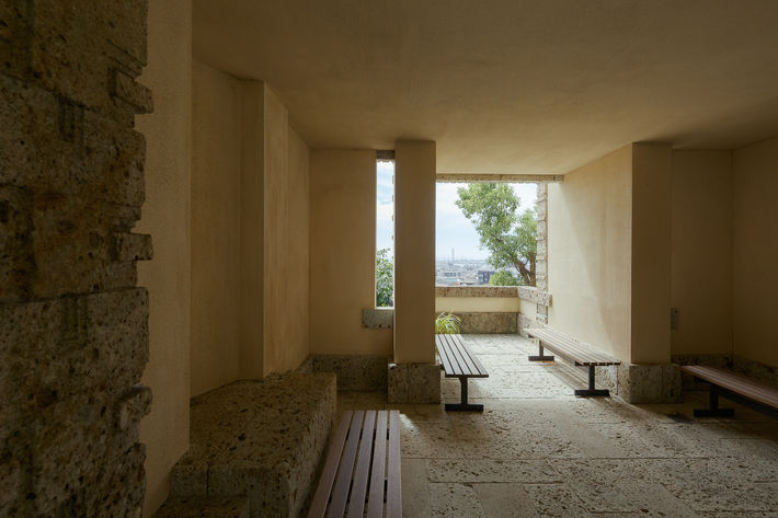 Interior view of the Yodoko Guest House designed by Frank Lloyd Wright, showcasing a serene seating area with stone benches and a window opening to the cityscape of Ashiya, Japan.