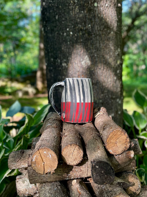 A black, white and red beer stein by Whitney Gill sitting atop a log pile, 2026.