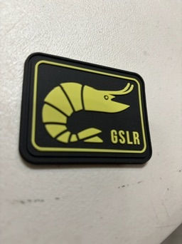 Black patch with a yellow prawn illustration and "GSLR" text on a white surface. Minimalist and quirky design.