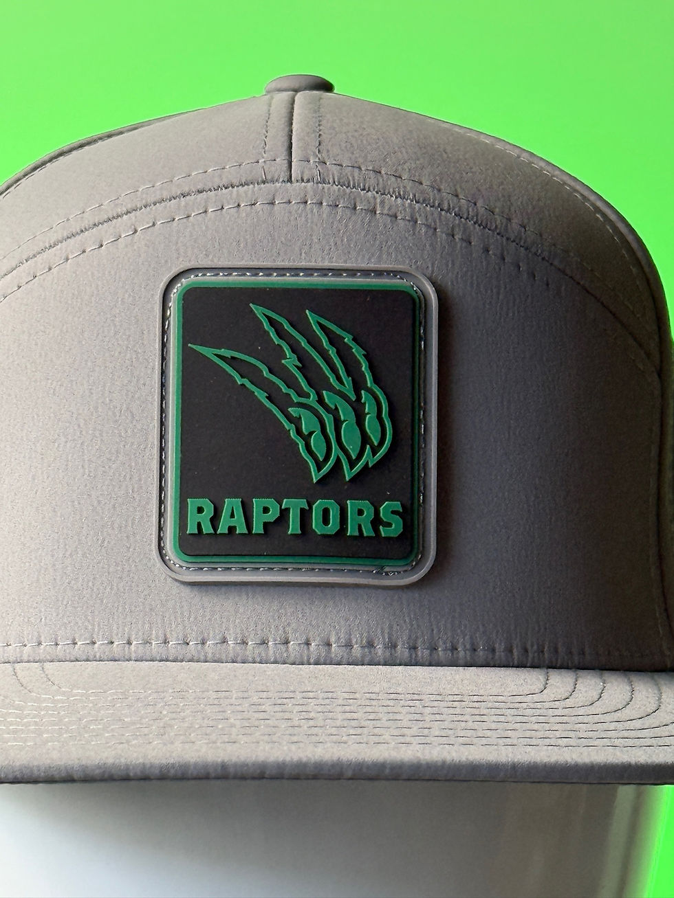 Gray cap with a Raptors logo featuring green claw marks. Bright green background enhances the design.